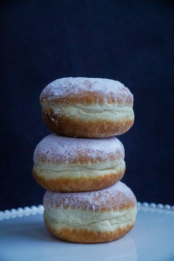 Three sugar-dusted fat round doughnuts sit on a white bed-edged plate. 